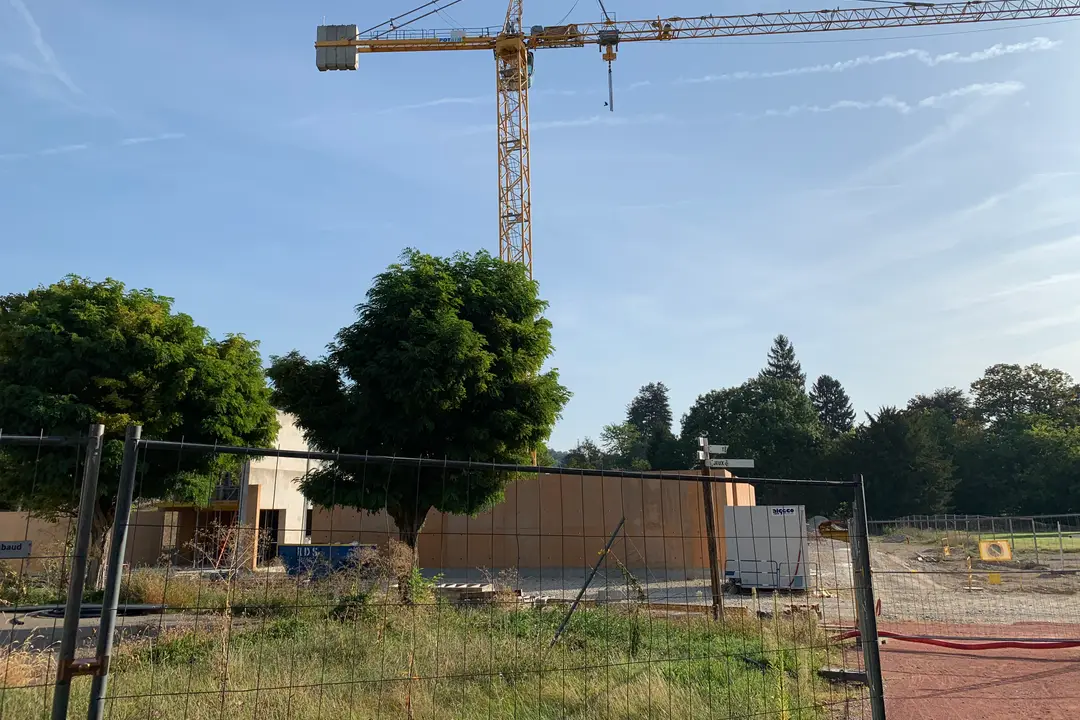 Mavi gökyüzü altında şantiye çitinin ardında yükselen kule vinç