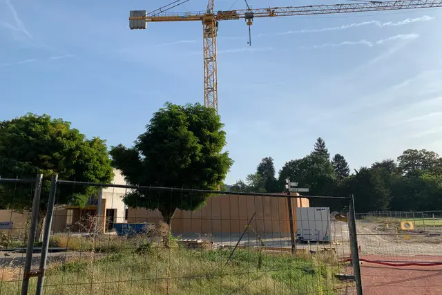 Mavi gökyüzü altında şantiye çitinin ardında yükselen kule vinç